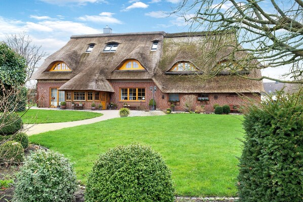 Une grande maison avec un toit de chaume, des murs en briques et une pelouse bien entretenue.