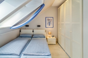 A bedroom with a skylight, two beds with patterned bedding, a bedside lamp, a framed picture, and a closet with louvered doors.