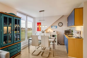 A modern kitchen with a dining area, a view through the window, and a clock on the wall.