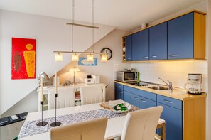 Une cuisine moderne avec des meubles bleus, un four à micro-ondes, une machine à café et un coin repas comprenant une table et des chaises.