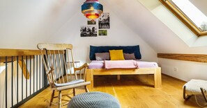 Un dormitorio tipo loft con techo inclinado, una cama de madera, una mecedora, una mesita y una lámpara colgante de colores.