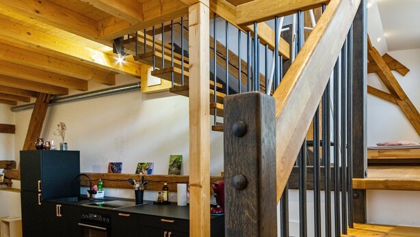 A wooden staircase with a metal railing, a kitchen area with a black refrigerator, and a wooden bench. - Apartment 'St Georgen 1' with Shared Terrace, Balcony and Wi-Fi (Freiburg im Breisgau)