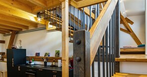 Una escalera de madera con barandilla metálica, una zona de cocina con un refrigerador negro y un banco de madera.