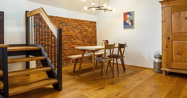 A room with a wooden staircase, a brick wall, a dining table with chairs, and a wooden cabinet. - Apartment 'St Georgen 1' with Shared Terrace, Balcony and Wi-Fi (Freiburg im Breisgau)