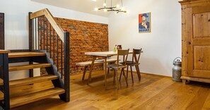 A room with a wooden staircase, a brick wall, a dining table with chairs, and a wooden cabinet.