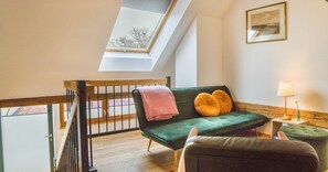 A loft bedroom with a green sofa, a pink blanket, a lamp, and a painting on the wall.