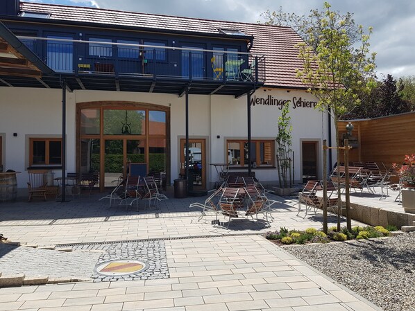 A building with a sign reading 'Wendlinger Coburg.' It features outdoor seating with tables and chairs, a paved courtyard, and a large glass entrance.