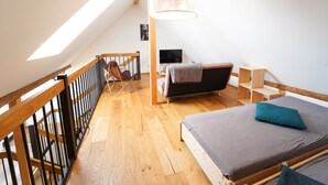 A loft bedroom with a sloped ceiling, a bed with a grey mattress and blue pillow, a wooden desk, a chair, and a television. - Apartment 'Wendlingen 3' with Shared Terrace, Balcony and Wi-Fi (Freiburg im Breisgau)