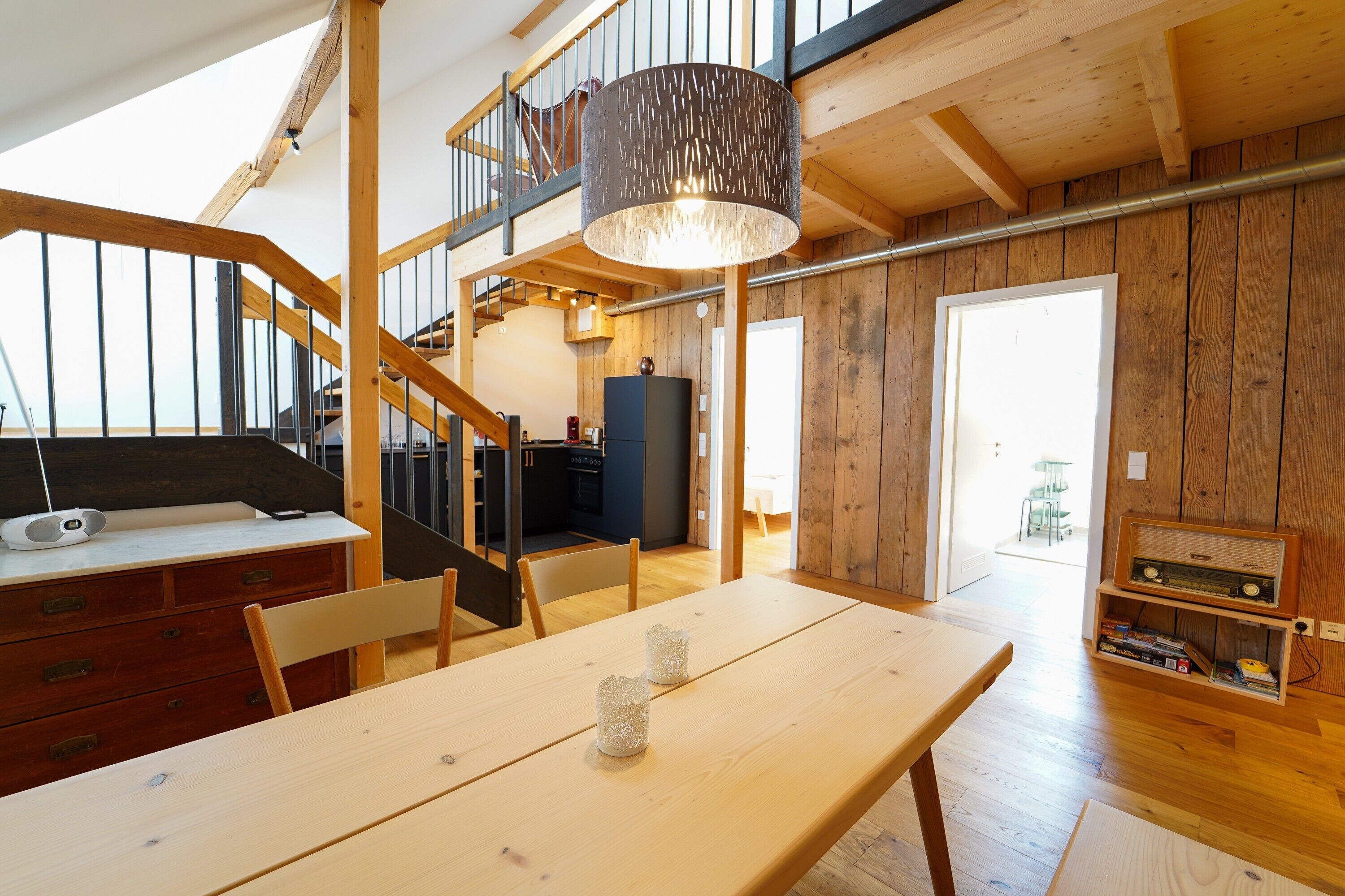 A wooden interior with a dining table, chairs, a staircase, and a radio.