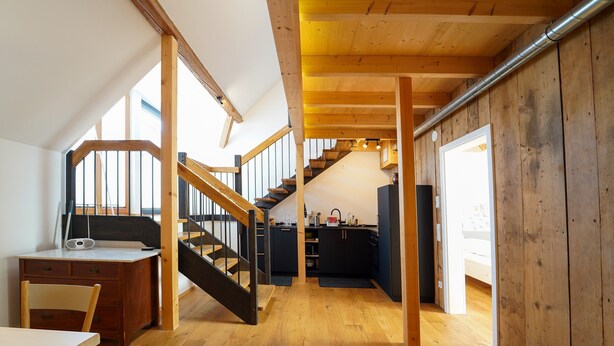 A loft-style room with a wooden staircase, a desk, and a view of the kitchen. - Apartment 'Wendlingen 3' with Shared Terrace, Balcony and Wi-Fi (Freiburg im Breisgau)