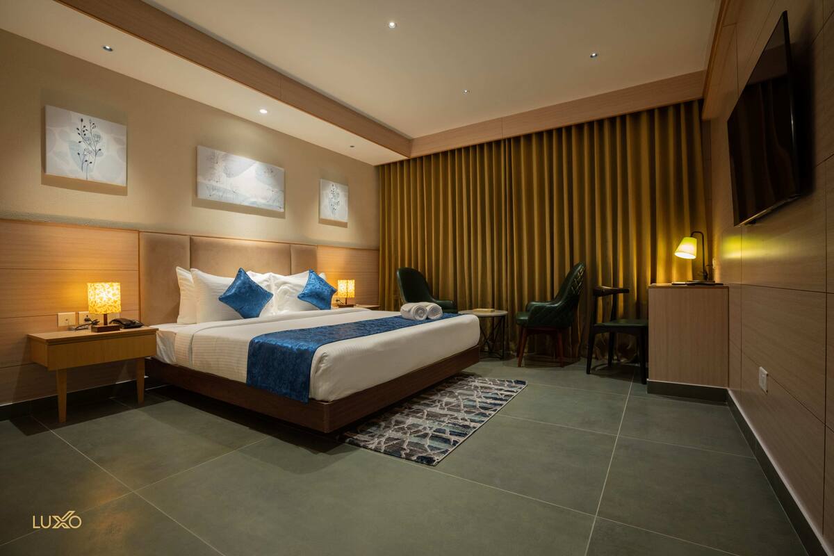 Una habitación de hotel moderna con una cama grande, mesitas de noche, un escritorio, una silla y un televisor montado en la pared.