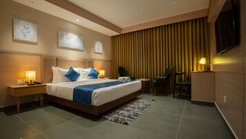 A modern hotel room with a large bed, bedside tables, a desk, a chair, and a TV mounted on the wall.