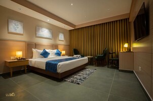 A modern hotel room with a large bed, bedside tables, a desk, a chair, and a TV mounted on the wall.
