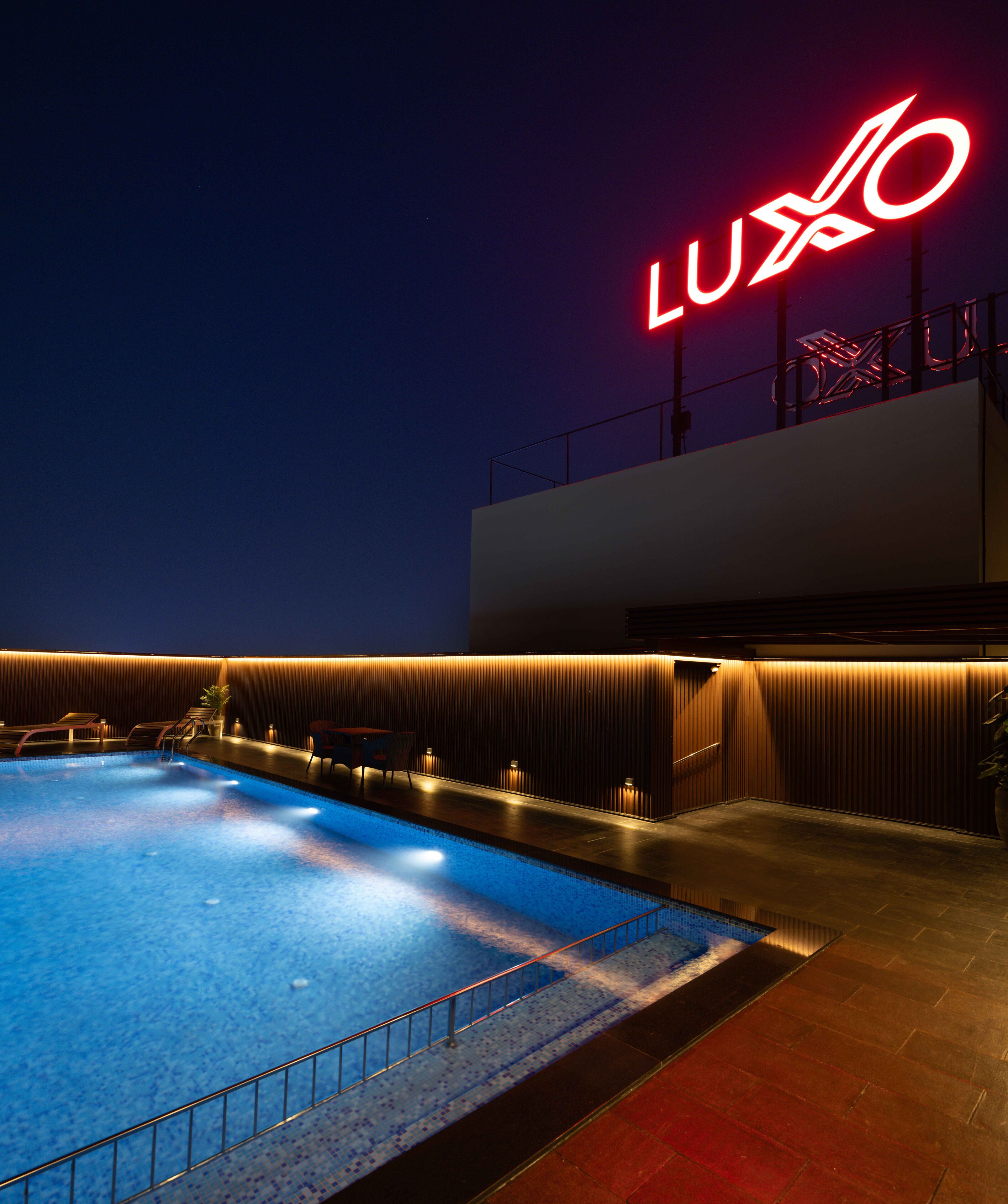 A swimming pool with a modern design, a neon sign, and a well-lit area with seating.
