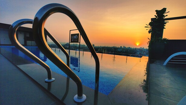 Une piscine sur le toit offrant une vue sur le coucher de soleil, des garde-corps en métal et une enseigne indiquant « LOYO by TOMORROW ».