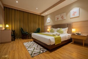 Habitación de hotel con una cama grande, un escritorio, dos sillas, una mesita de noche y obras de arte en las paredes.