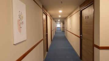 Pasillo de hotel con puertas de madera, alfombra azul y una lámpara en el techo.
