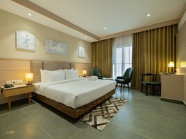 A hotel room with a large bed, two chairs, a desk, and a window with curtains.
