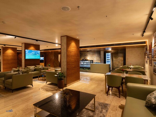 A modern hotel lobby with a reception desk, seating area, and a large flat-screen TV. - Luxo Kochi (Kanayannur)