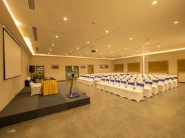 A conference room with rows of white chairs, a podium, and a projector screen.