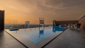 Una piscina infinita en la azotea con vistas a la ciudad, un cartel que dice 'LUXO' y mobiliario de exterior.