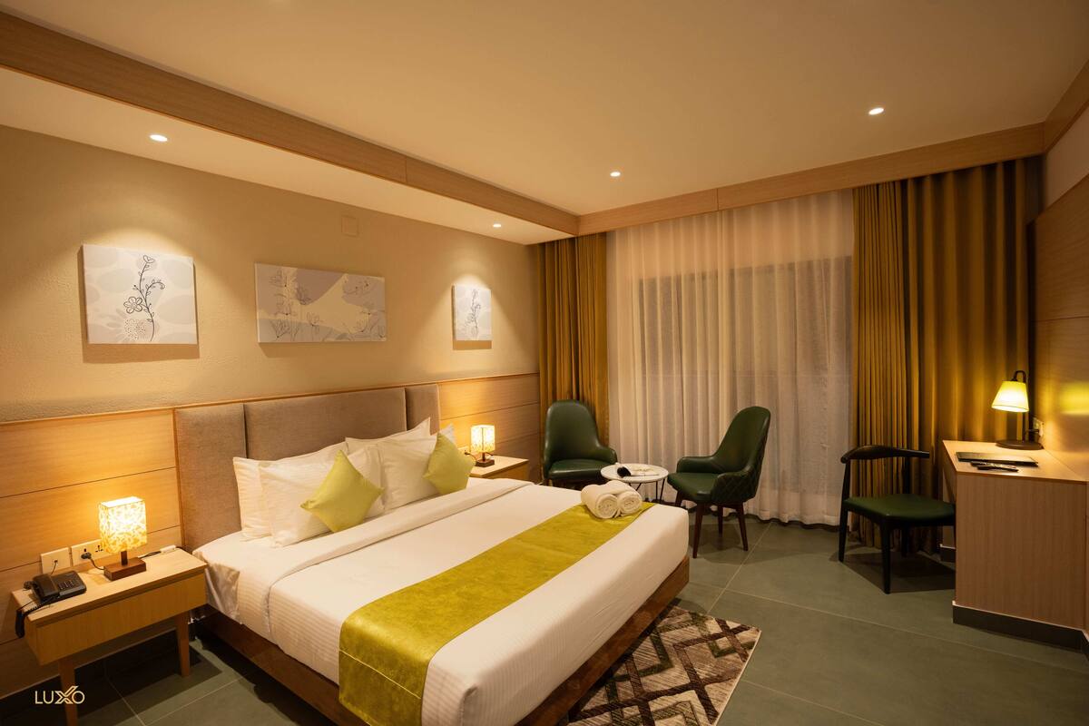 Habitación de hotel con cama, dos sillas, escritorio y mesita de noche con lámpara.
