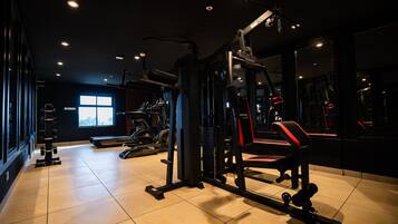 Un gimnasio con diversos equipos de ejercicio, una cinta de correr y un ventanal que proporciona luz natural.