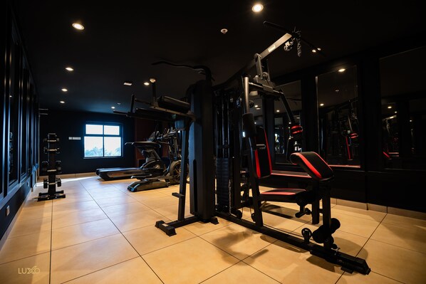 Un gimnasio con diversos equipos de ejercicio, una cinta de correr y un ventanal que proporciona luz natural.