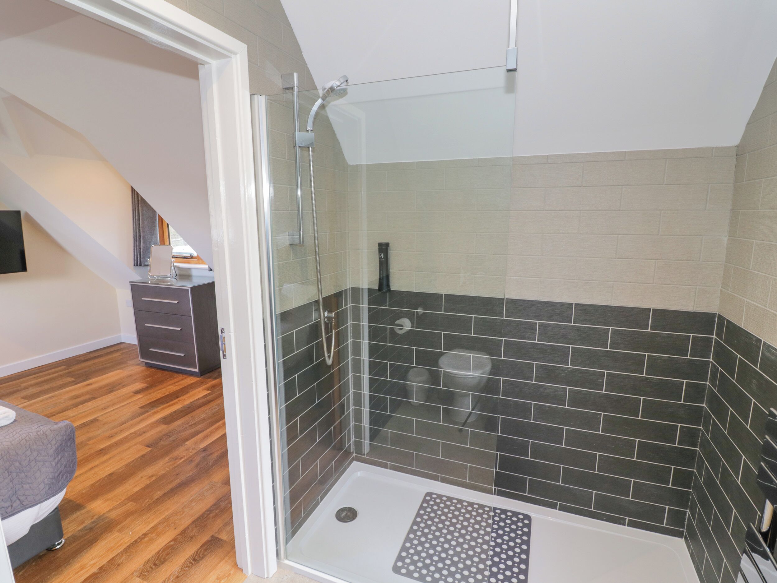 Een moderne badkamer met een douchecabine van glas, donkere betegelde wanden en een houten vloer.