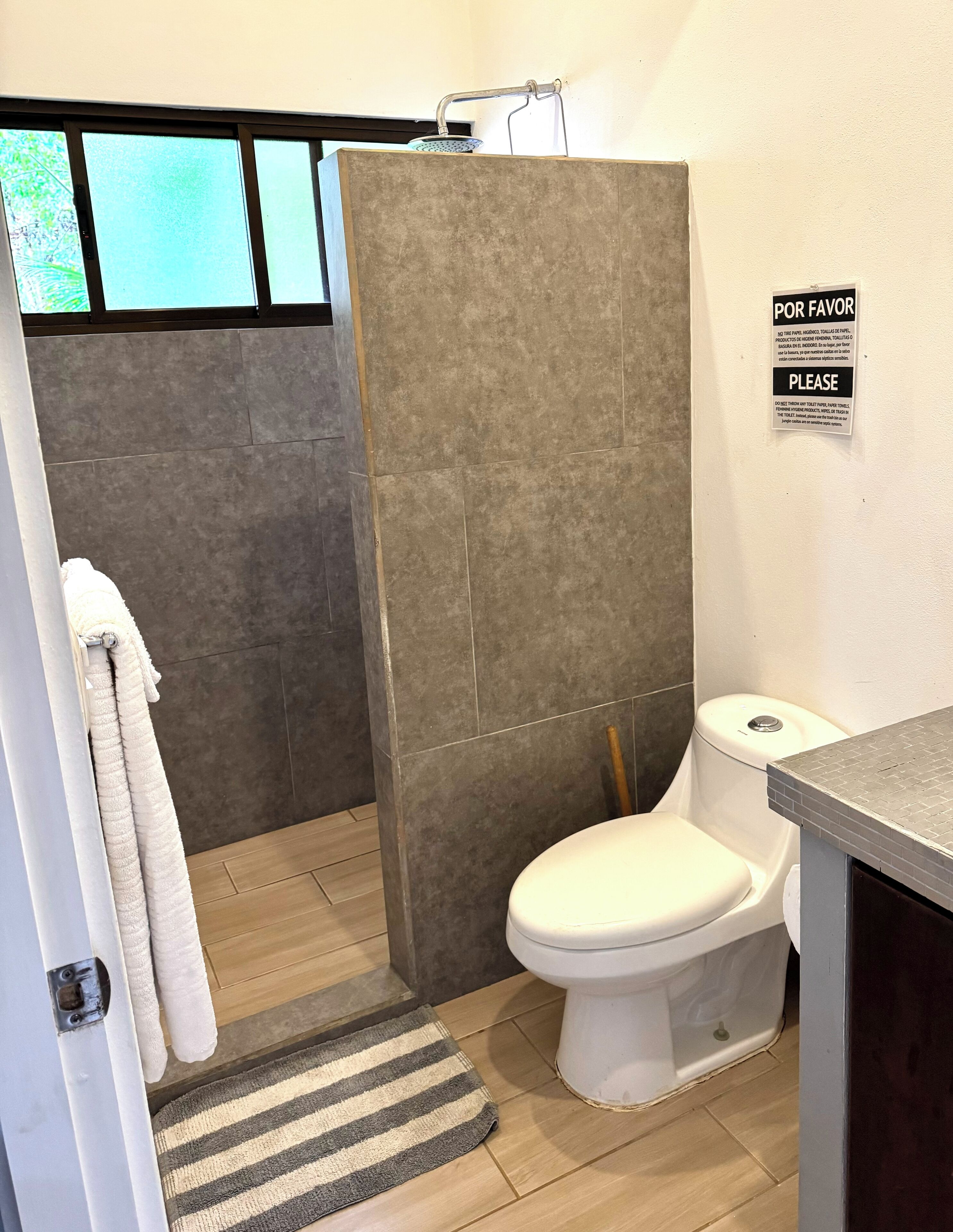 Une salle de bain avec une douche, des toilettes et un panneau indiquant : « POR FAVOR PLEASE ».