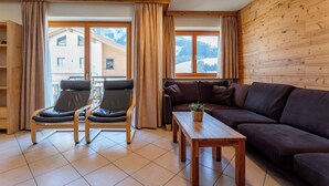 A cozy living room with a wooden wall, a brown sofa, two leather chairs, a wooden coffee table, and a view of a snowy mountain through large windows. - Superb apartment on the slopes with terrace (Hinterglemm)