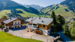A modern two-story building with a flat roof, a covered outdoor area, and a view of a mountainous landscape. - Superb apartment on the slopes with terrace (Hinterglemm)