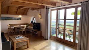 Una habitación acogedora con techo de madera, una zona de comedor con mesa y sillas, televisor y ventanas grandes con cortinas.