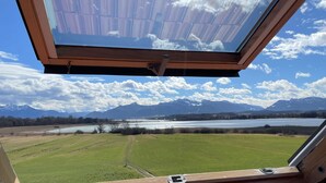 Una habitación con un tragaluz amplio que da a un paisaje pintoresco con un lago y montañas.
