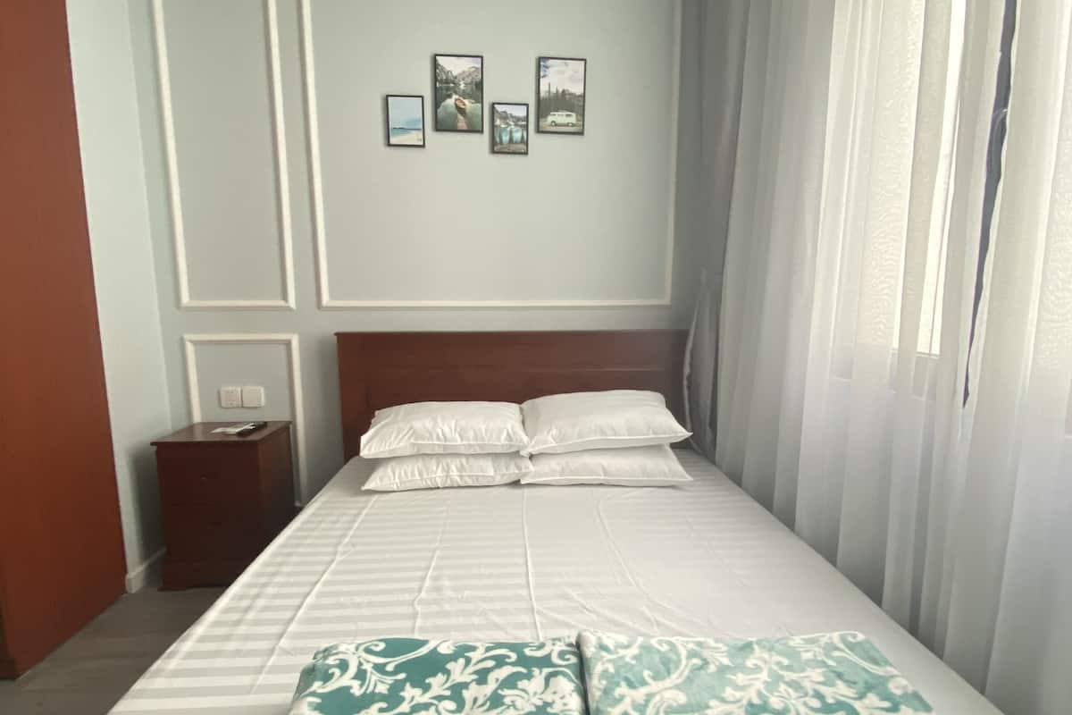 A neatly made bed with a patterned blanket, a wooden headboard, and a nightstand with a remote control. There are framed pictures on the wall above the bed.