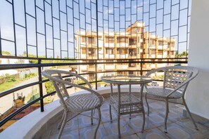 Un balcon doté de fauteuils en osier et d’une table en verre, offrant une vue sur un immeuble à multiples balcons.