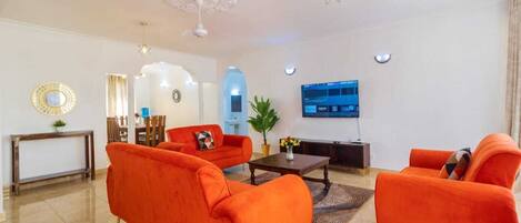 A modern living room with orange sofas, a coffee table, a TV, and decorative elements like a mirror and plants.