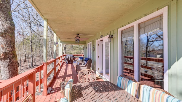 Une terrasse couverte avec des sièges d’extérieur, un ventilateur de plafond et une vue sur les arbres environnants.