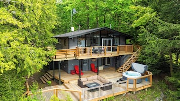 A two-story cabin with a deck, outdoor seating, and a hot tub.