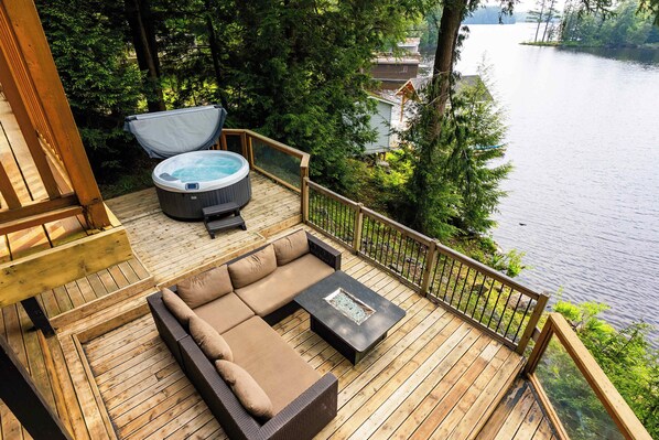 A wooden deck with a hot tub, a sofa, and a table.