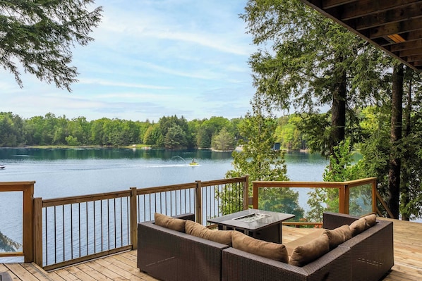 A deck with wicker furniture, a table, and a view of a lake with boats.