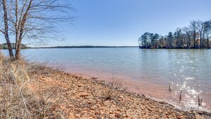 Vista de un lago con orilla arenosa, árboles y cielo despejado.