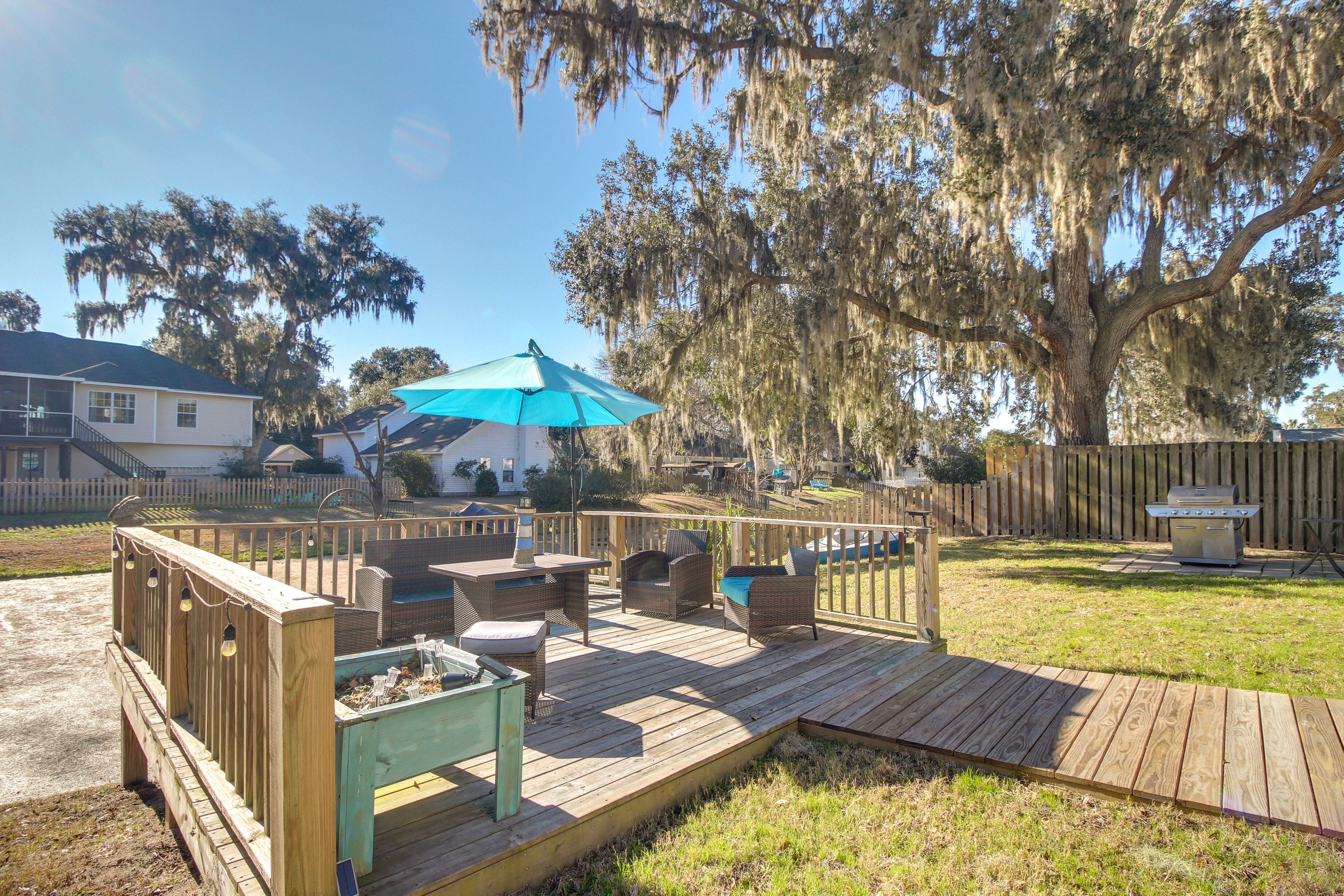 A wooden deck with outdoor furniture, a barbecue grill, and a large tree with Spanish moss.