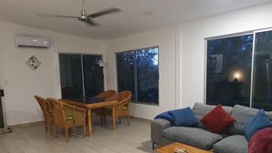 Una sala de estar con sofá gris, una mesa de centro de madera, sillas de mimbre y una mesa de comedor.