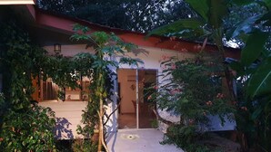 Una casa con porche cubierto, una puerta que da a un espacio interior y un pequeño jardín con grava y plantas.