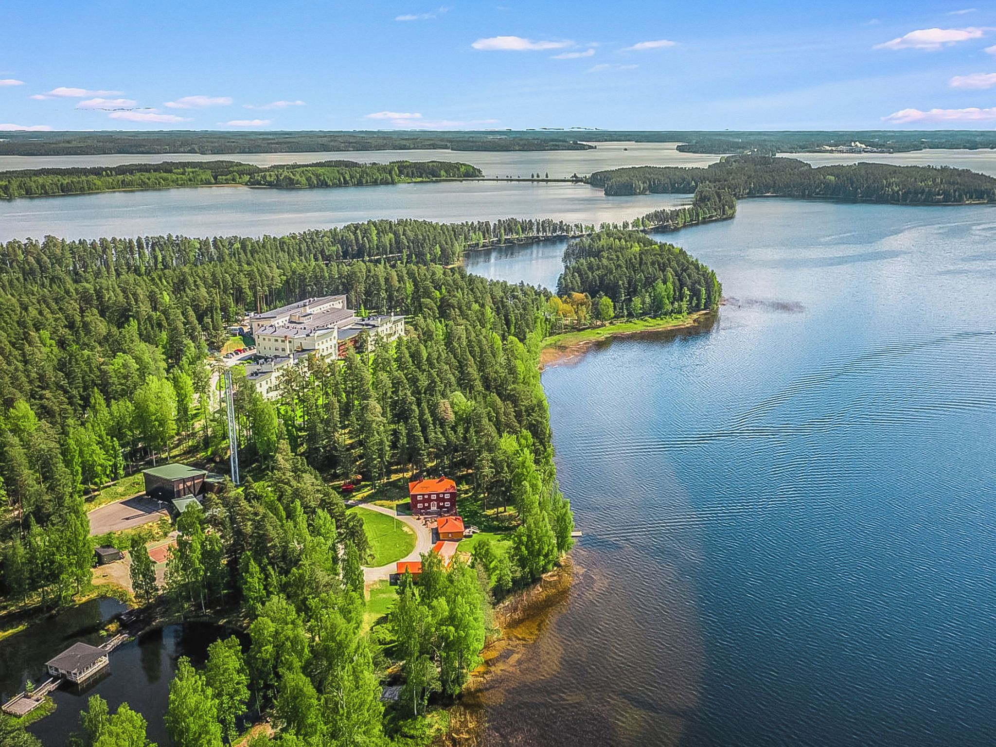 Vista aérea de una propiedad junto al lago, con un bosque denso, un edificio principal y una construcción más pequeña.