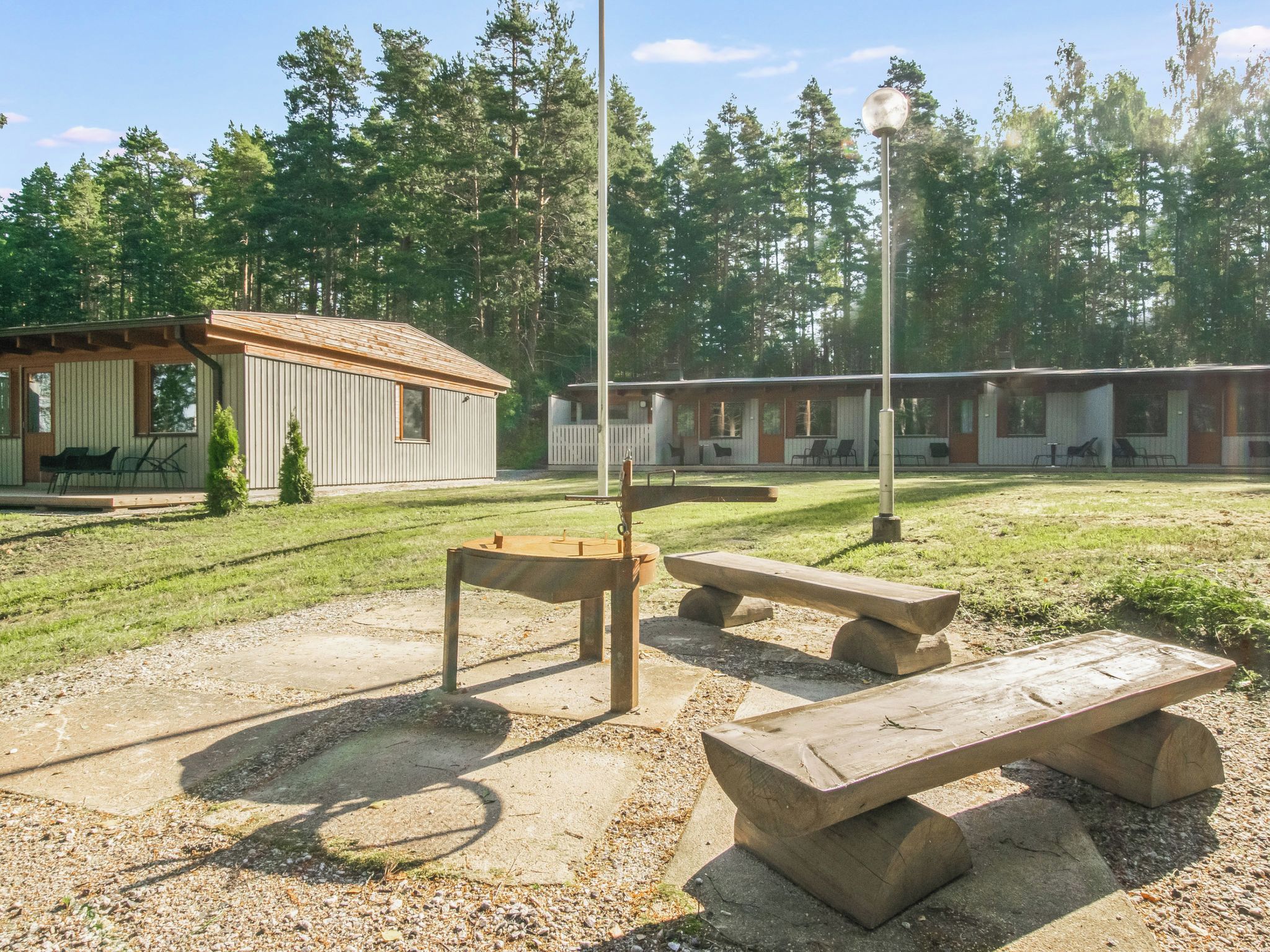 A picnic area with benches and a table, surrounded by a grassy field and a row of cabins.