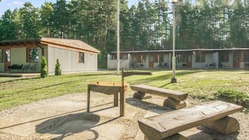 A picnic area with benches and a table, surrounded by a grassy field and a row of cabins.