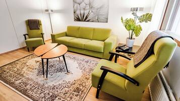 A living room with a green sofa, a round coffee table, a small side table, a potted plant, and a radiator.