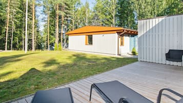 Puinen terassi, jossa on kaksi aurinkotuolia, pieni punakattoinen rakennus ja valkoinen aita.